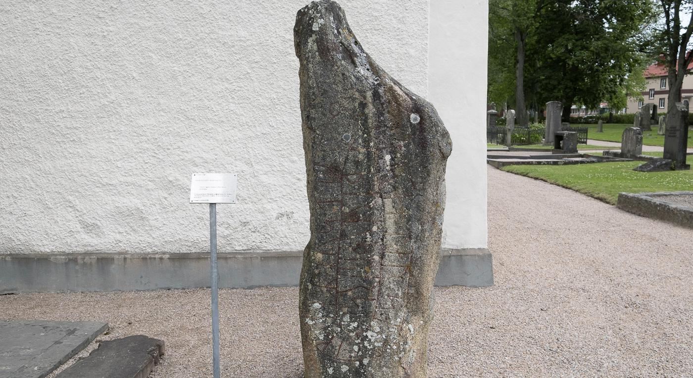 En stor runsten framför en vit kyrkbyggnad.