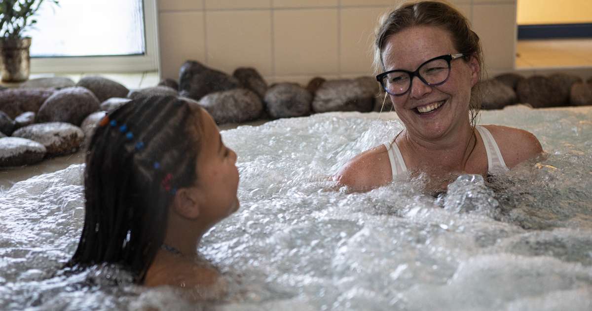 En mor och en dotter sitter i en bubbelpool och ler mot varandra.