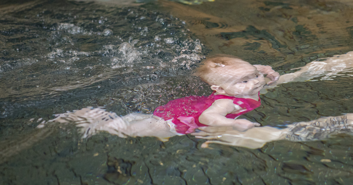 En bebis får hjälp att ta sig fram under vattenytan.