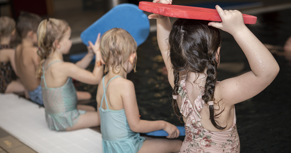 En grupp unga flickor som sitter bredvid varandra i en simbassäng.