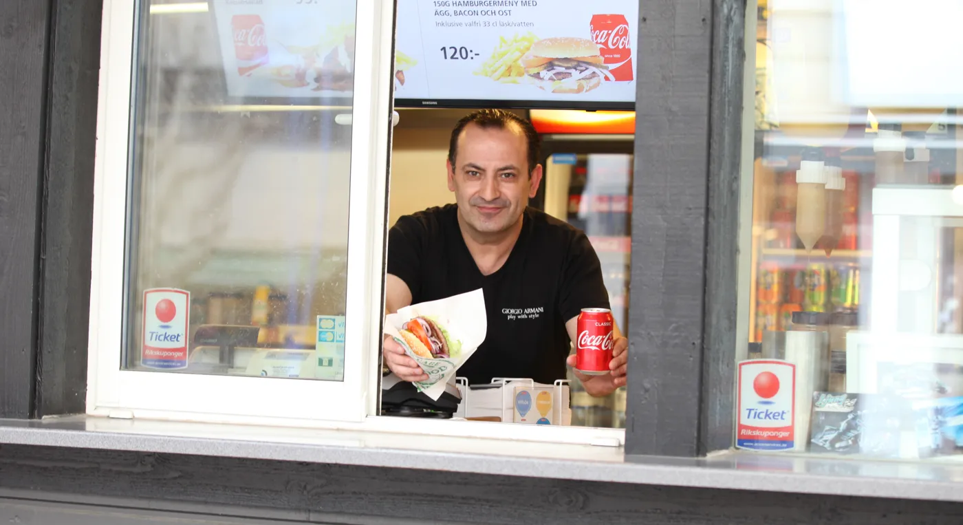 En man räcker ut en hamburgare och en läskburk genom en kiosklucka.